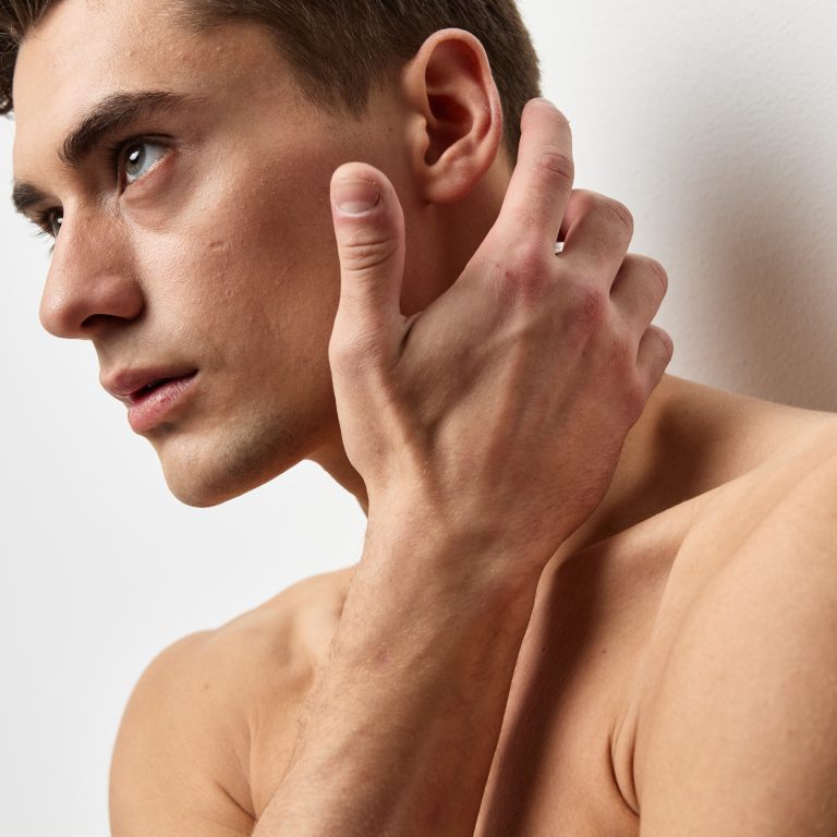 A sexy guy with a naked torso touches his face with his hand and looks to the side. High quality photo
