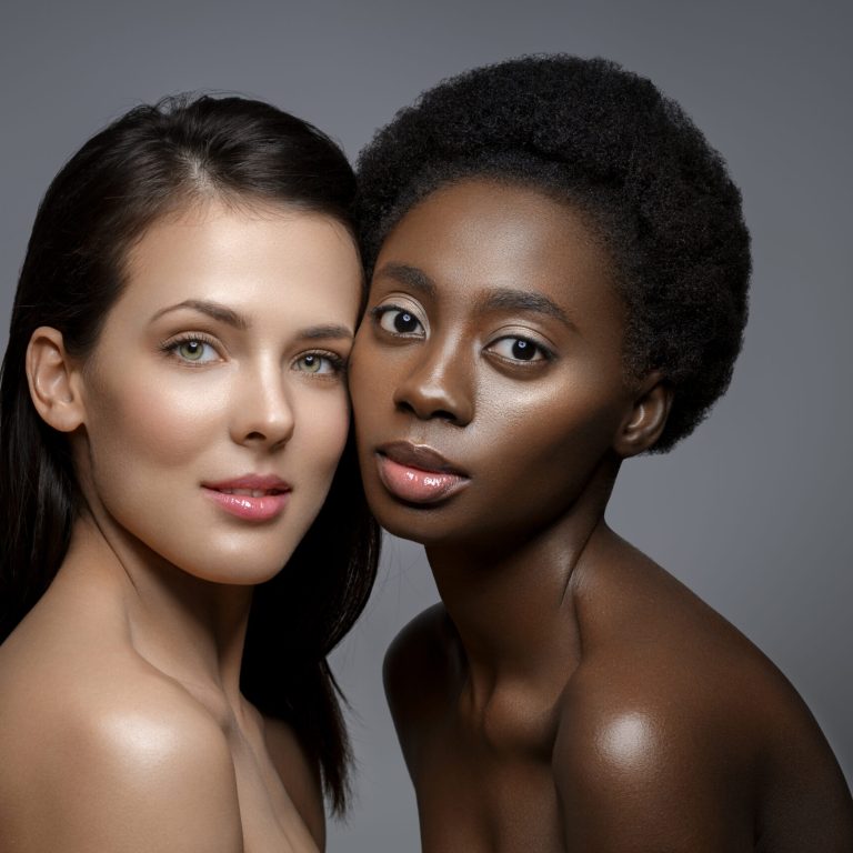 Beautiful young black woman with natural make up and glowing skin in white veil fashion hat. Beauty shot on grey background. Copy space.