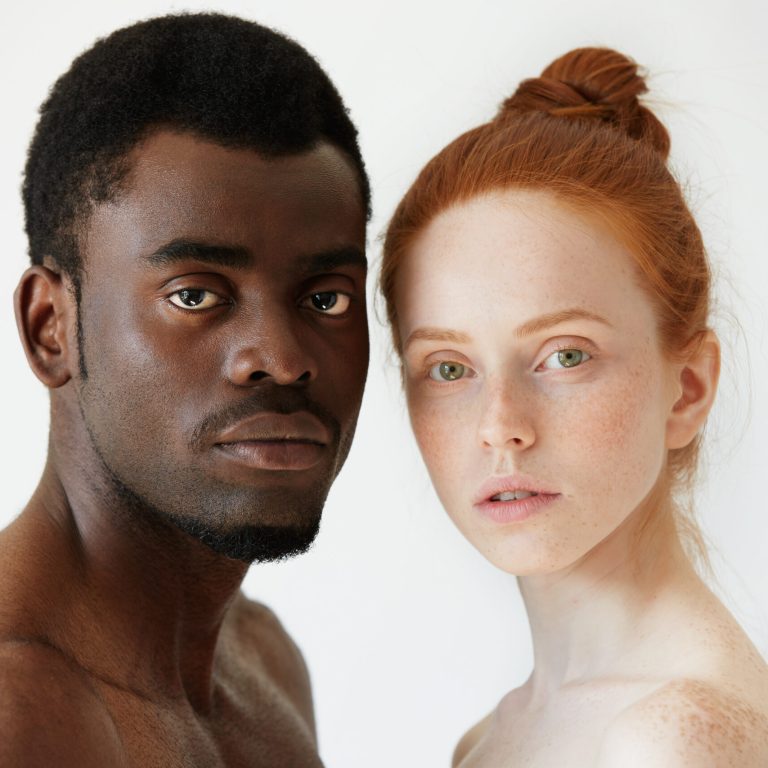 Black and white. Headshot of African man and Caucasian woman standing shirtless and looking at the camera with serious expression. Portrait of young beautiful interracial couple. Mixed race relations