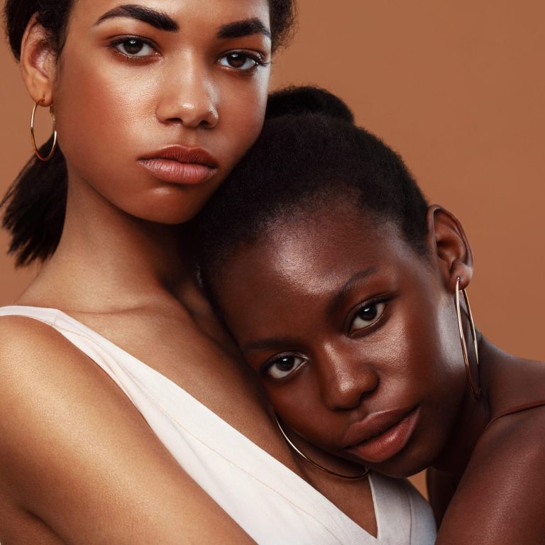 Two beautiful women standing in studio and looking at camera. Young woman relaxing on girlfriend's chest.
